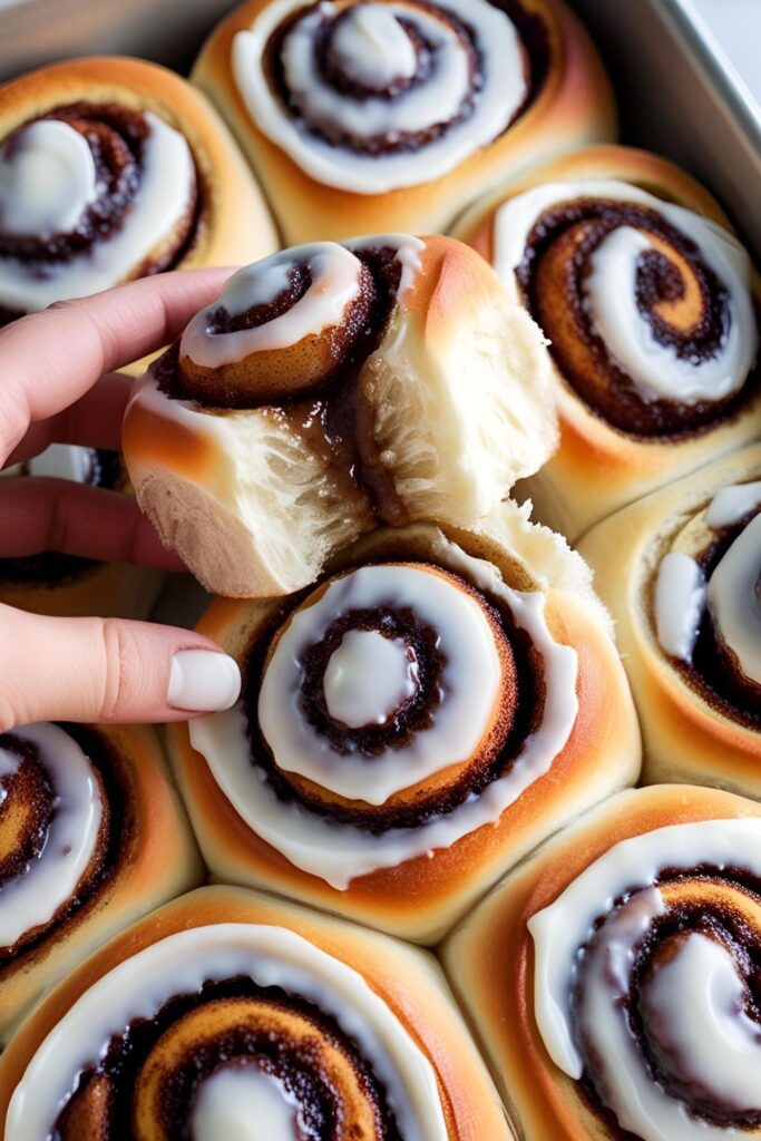 Close-up of a cinnamon roll being pulled apart to reveal gooey, cinnamon-sugar swirls inside.