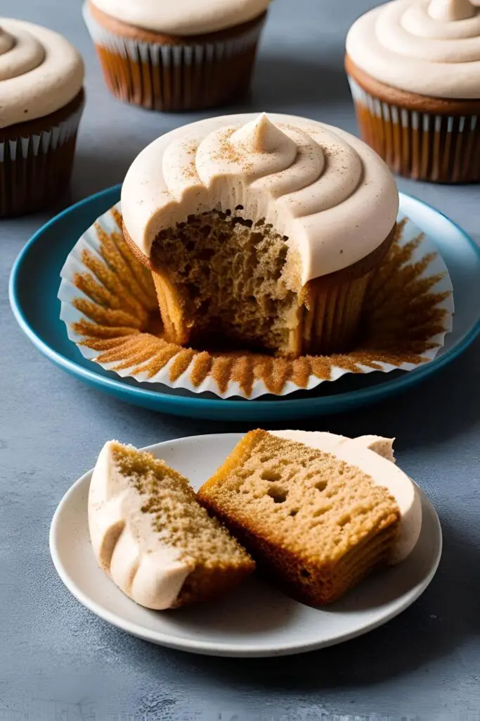 "Homemade chai latte cupcakes topped with whipped frosting and dusted with cinnamon, displayed on a rustic wooden surface."