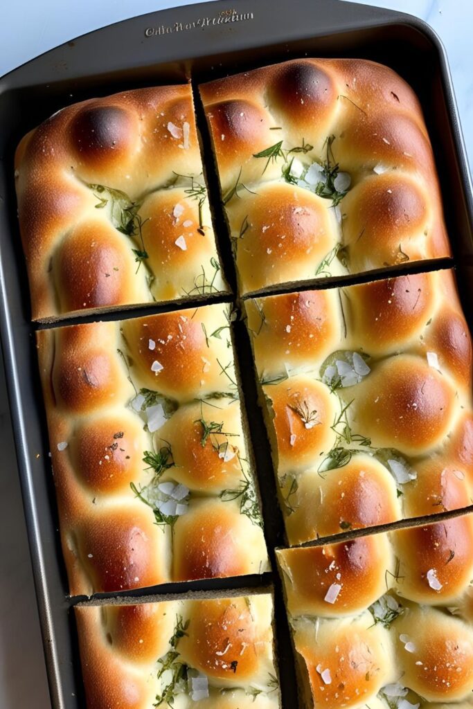 Sliced herb focaccia on a wooden board, showcasing its airy texture and herb topping.