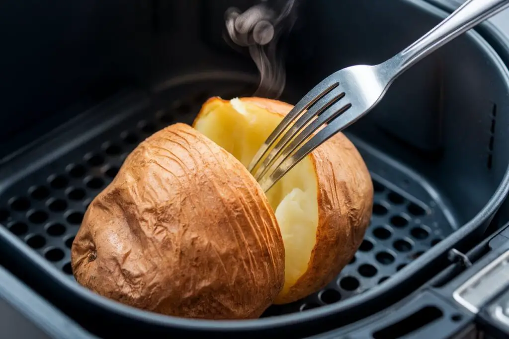 A golden-brown baked potato being tested for doneness with a fork in an air fryer basket