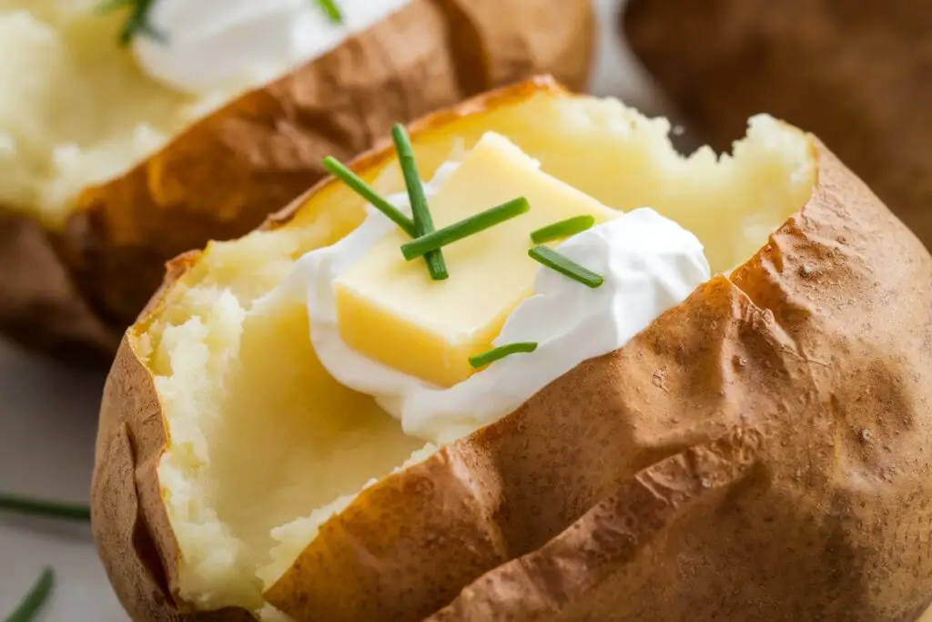 A perfectly cooked air fryer baked potato, split open and topped with butter and sour cream.