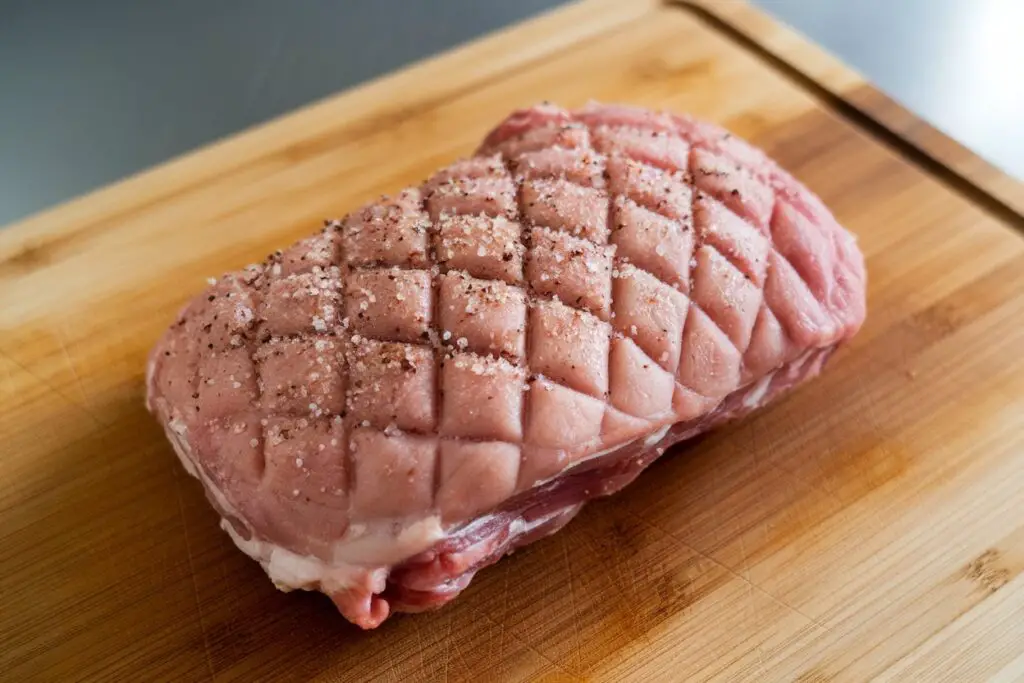 Raw pork knuckle, scored and seasoned, ready for cooking.