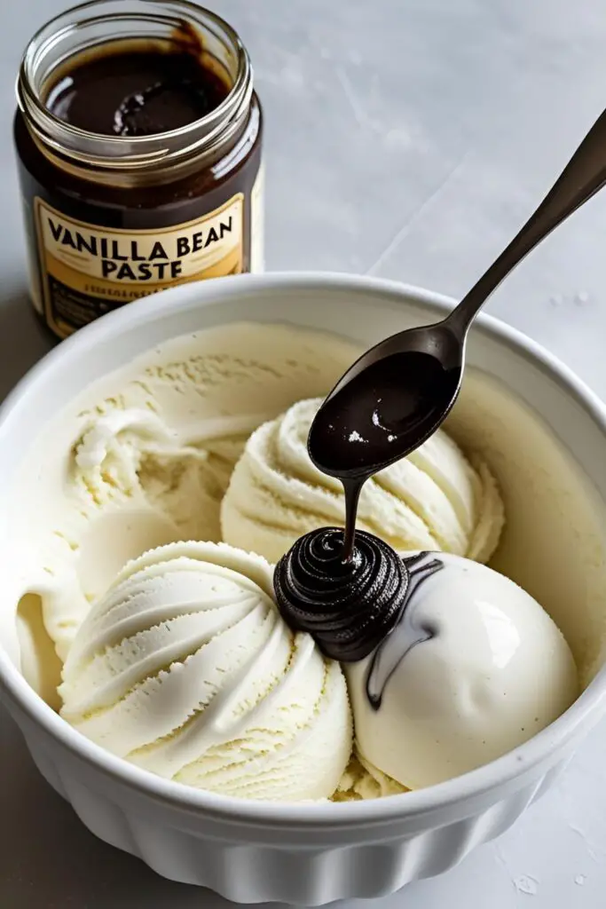 A jar of homemade vanilla bean paste, with a spoonful being added to a white ice cream base